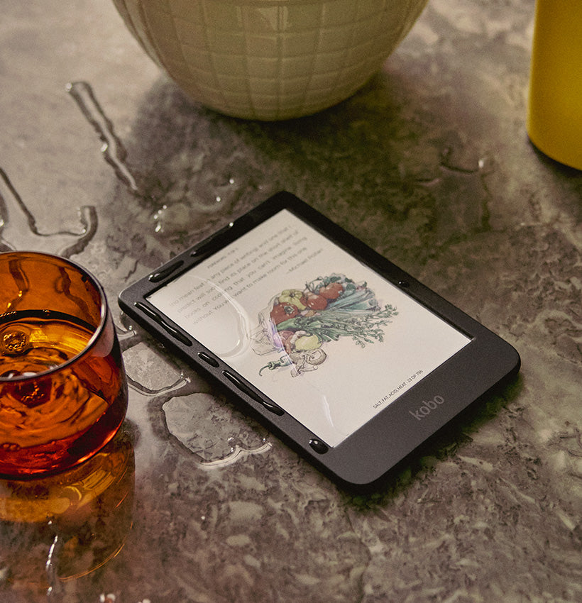A Kobo Clara Colour eReader set on a marble counter, with water spilled on it. Its screen shows a colour image from a cookbook.